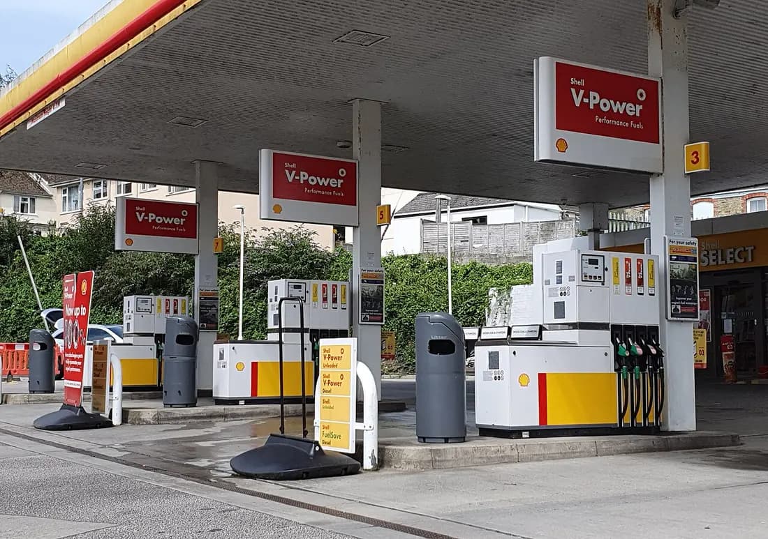Rows of fuel pumps with nozzles, price displays and grade labels (V-Power, Unleaded, Diesel) under the canopy of a Shell petrol station in Truro, Cornwall.